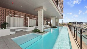 A swimming pool with a view of the cityscape, surrounded by a modern building with a patterned wall and a glass railing. - 2 bed  2 bath Pool Car Park (Mermaid Beach)