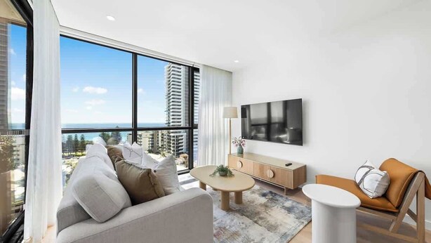 A modern living room with a sofa, armchair, coffee table, and TV. - 2 bed  2 bath Pool Car Park (Mermaid Beach)