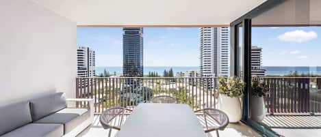 A balcony with a table and chairs, a sofa, and a view of tall buildings and the sea.