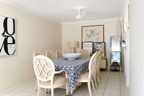 Un coin repas avec une table dressée pour quatre personnes, entouré de chaises en osier, d’un ventilateur de plafond et d’œuvres d’art murales.