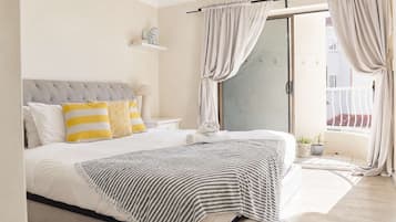 A bedroom with a bed, curtains, a nightstand, a lamp, and a view of the outside.