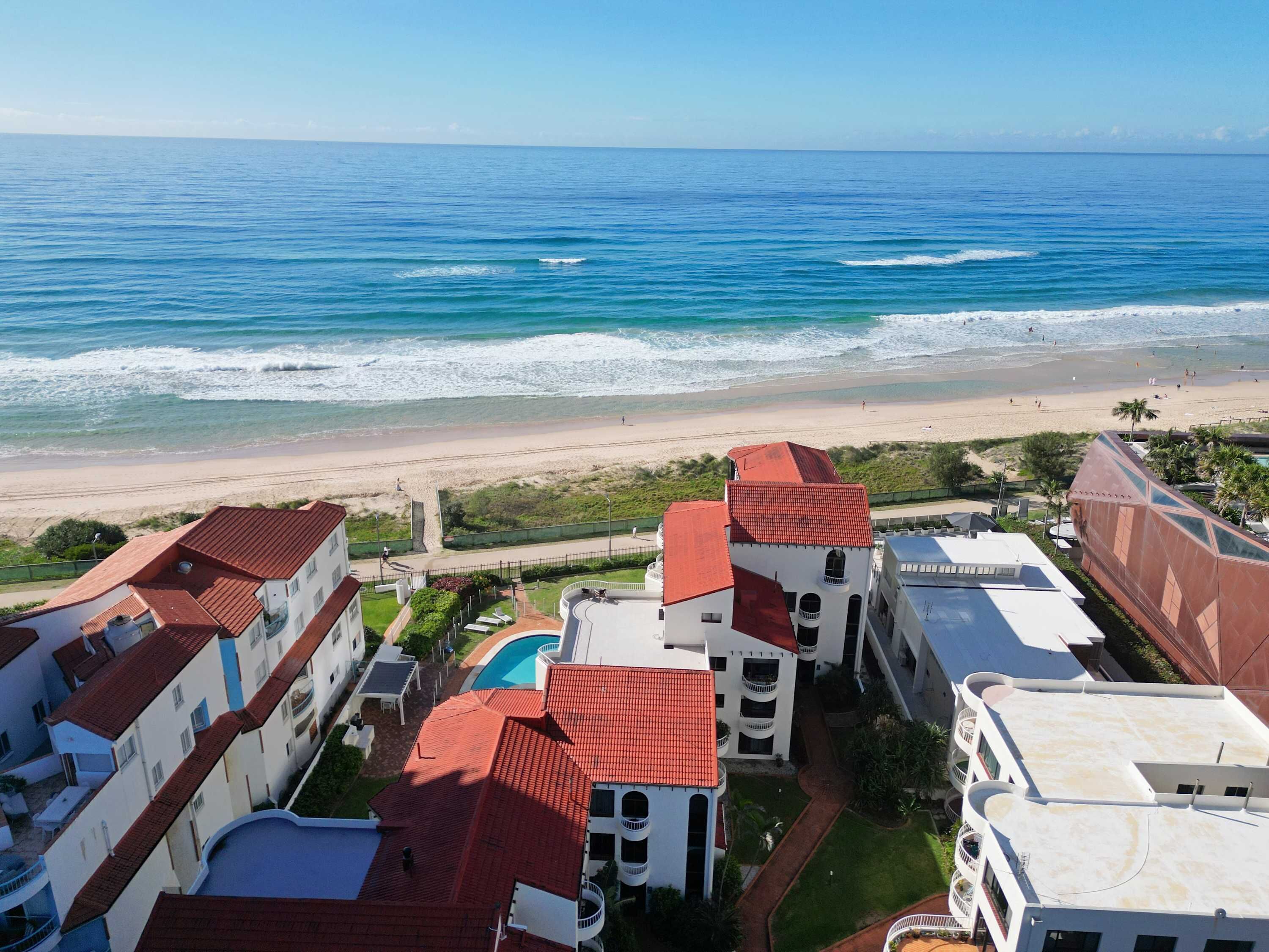 A coastal hotel with multiple buildings, a swimming pool, and a beach view.