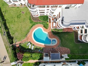 A high-rise building with a central courtyard featuring a swimming pool, surrounded by green lawns and a brick pathway. - Mykonos Absolute Beachfront Apt Parking Ocean Views Pets Welcome (Surfers Paradise)