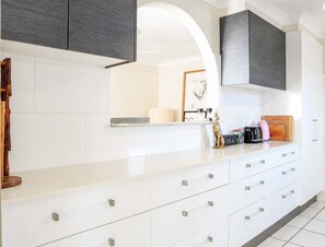 Une cuisine moderne avec des meubles blancs, un grand îlot central doté de tiroirs, une machine à café et une planche à découper en bois.