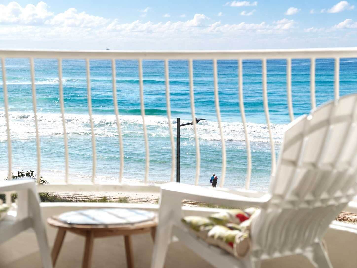 A balcony with a view of the ocean, a chair, and a small table.