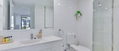 A modern bathroom with a large mirror, a white sink, a toilet, and a glass-enclosed shower.