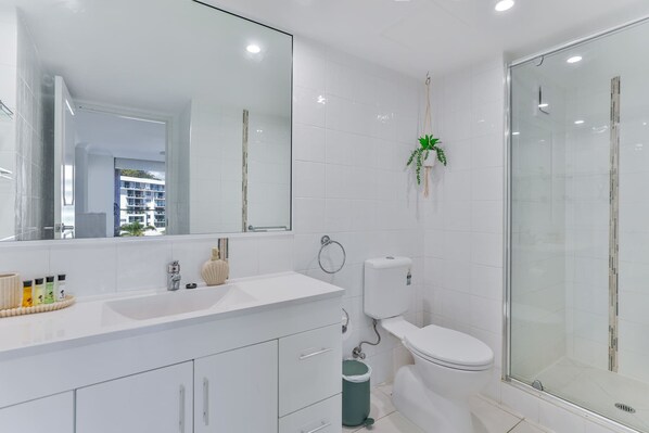 Une salle de bain moderne avec un grand miroir, un lavabo blanc, des toilettes et une douche à parois de verre.
