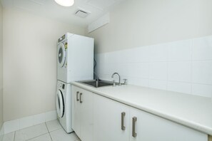 A compact kitchen with a built-in washing machine, a sink, and cabinets. - 3BR Opposite Burleigh Beach  Pool  Car Park (Burleigh Heads)