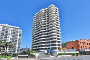 Un edifici alt amb nombroses balcons, cel serè i un carrer amb un senyal de límit de velocitat.