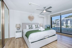 A modern hotel room with a large bed, a ceiling fan, a heart-shaped wall decoration, and a view of a building complex. - 3BR Opposite Burleigh Beach  Pool  Car Park (Burleigh Heads)