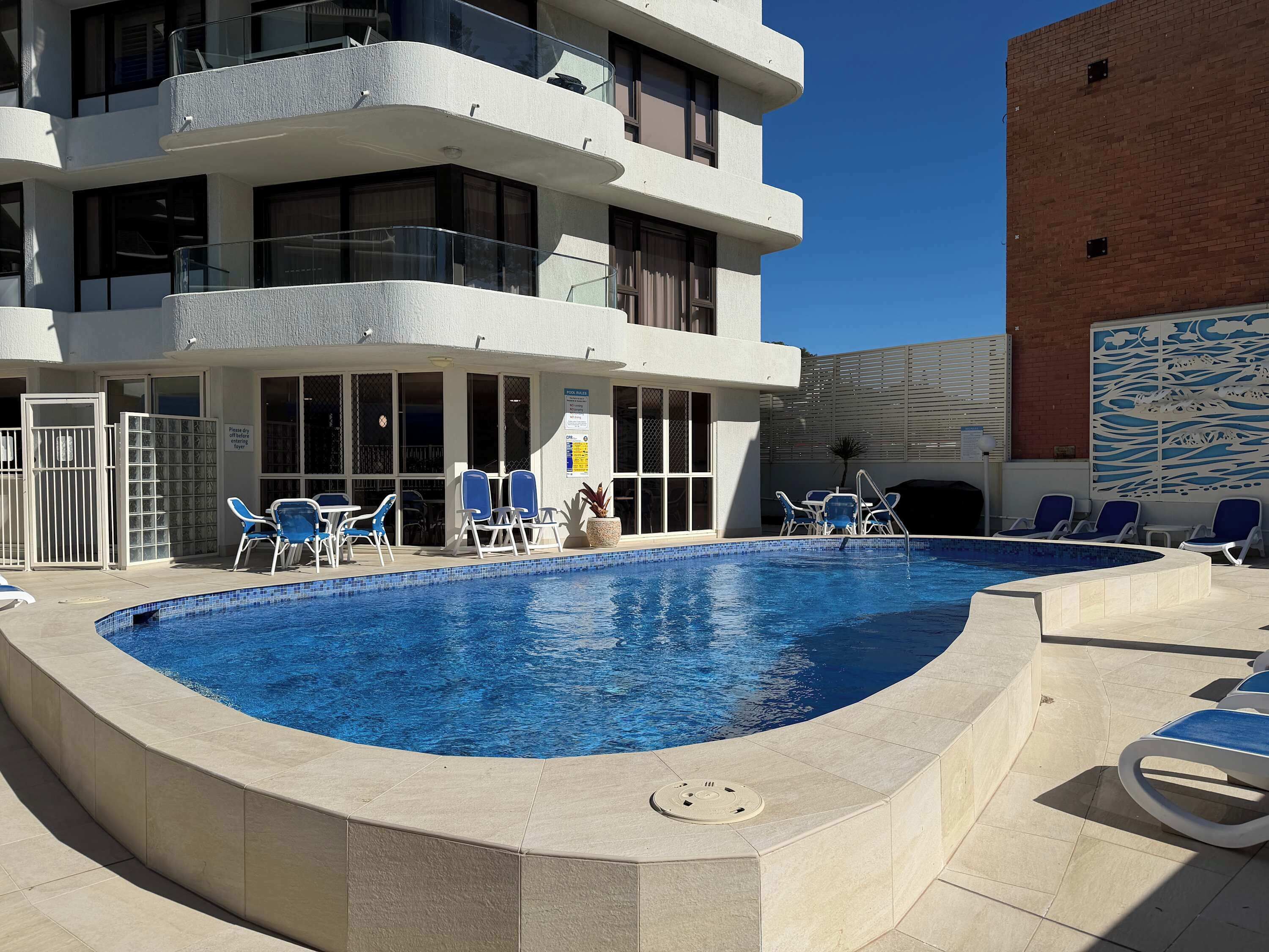 A swimming pool with lounge chairs and a building with multiple balconies.