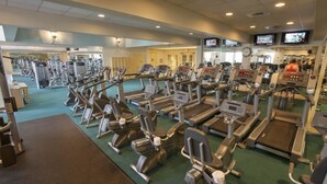Une salle de sport équipée de divers appareils d’exercice, notamment des tapis de course et des vélos elliptiques, disposés en rangées.
