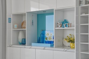 A white shelving unit with various decorative items, including a blue vase, a blue bottle, and a sign that reads 'SUN SEA SAND'. - Lvl 15 Sunrise + Sunset Views | Pool + Parking (Surfers Paradise)