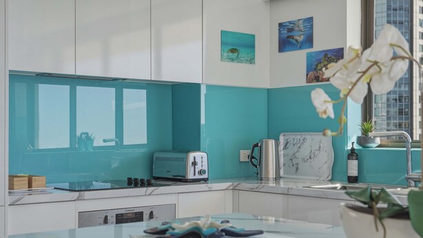A modern kitchen with teal backsplash, white cabinets, a toaster, a kettle, and a marble countertop. - Lvl 15 Sunrise + Sunset Views | Pool + Parking (Surfers Paradise)