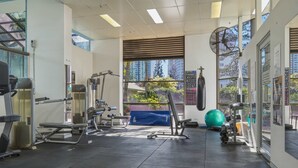 A gym with various exercise equipment, large windows, and a view of buildings outside. - Lvl 15 Sunrise + Sunset Views | Pool + Parking (Surfers Paradise)