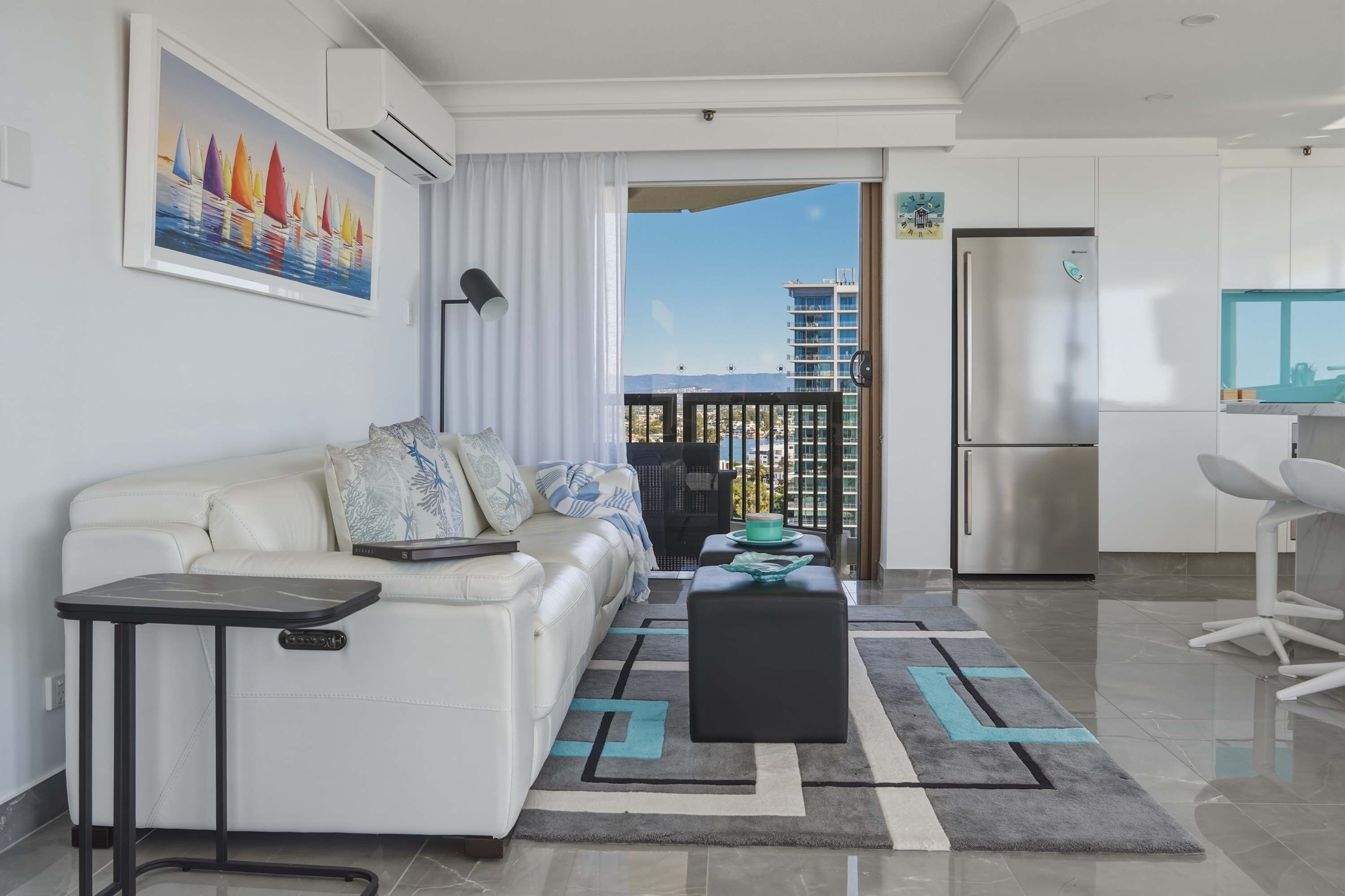 Een moderne woonkamer met een bank, een bijzettafeltje en uitzicht op een stadslandschap via een balkon.