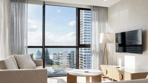Et moderne hotelværelse med et stort vindue, et fladskærms-tv, en sofa, et lille bord og et skab.