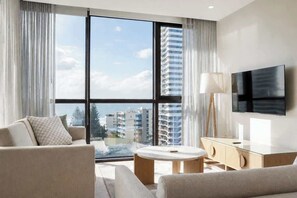 Ein modernes Hotelzimmer mit großem Fenster, Flachbildfernseher, einer Couch, einem kleinen Tisch und einem Schrank.