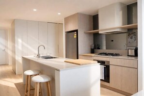 A modern kitchen with a central island, bar stools, and built-in appliances. - 2BR Ocean Views Pool Gym Sauna (Mermaid Beach)