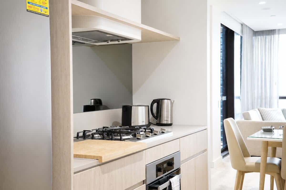 A modern kitchen with a gas stove, kettle, and oven, leading to a dining area with a table and chairs.