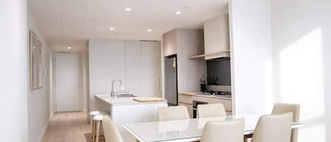 A modern kitchen with white cabinetry, a central island, and a dining area with a white table and chairs.