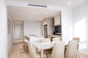 Uma cozinha moderna com armários brancos, uma ilha central e um espaço de jantar com mesa e cadeiras brancas.