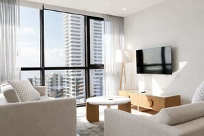 A modern hotel room with a large window, a flat-screen TV, a round coffee table, and a wooden cabinet. - 2BR Ocean Views Pool Gym Sauna (Mermaid Beach)