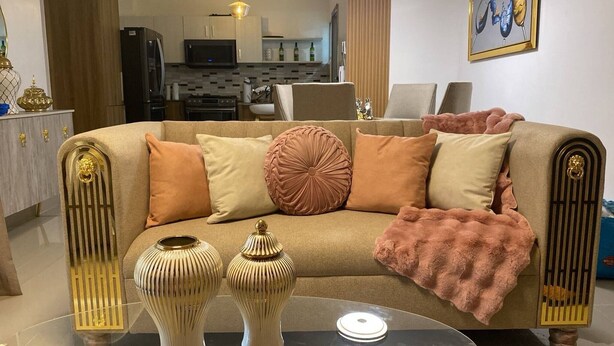 A living room with a sofa, decorative vases, and a kitchen in the background. - Spacious Condo With Pool, Gym, and Central AC in Santiago (Puñal)