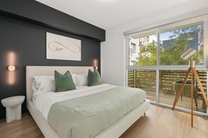 Un dormitorio moderno con una cama grande, una mesita de noche, una obra de arte abstracta infinita en la pared y vistas al exterior a través de un ventanal amplio.