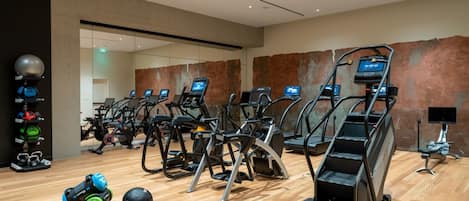 A modern gym with multiple treadmills, weightlifting equipment, and a wooden floor.