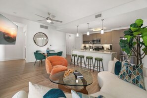 Una sala de estar moderna con una mesa de centro de vidrio, un sofá y un comedor con una silla y taburetes.
