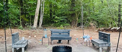 A forested area with a seating arrangement including benches and a table, surrounded by trees.