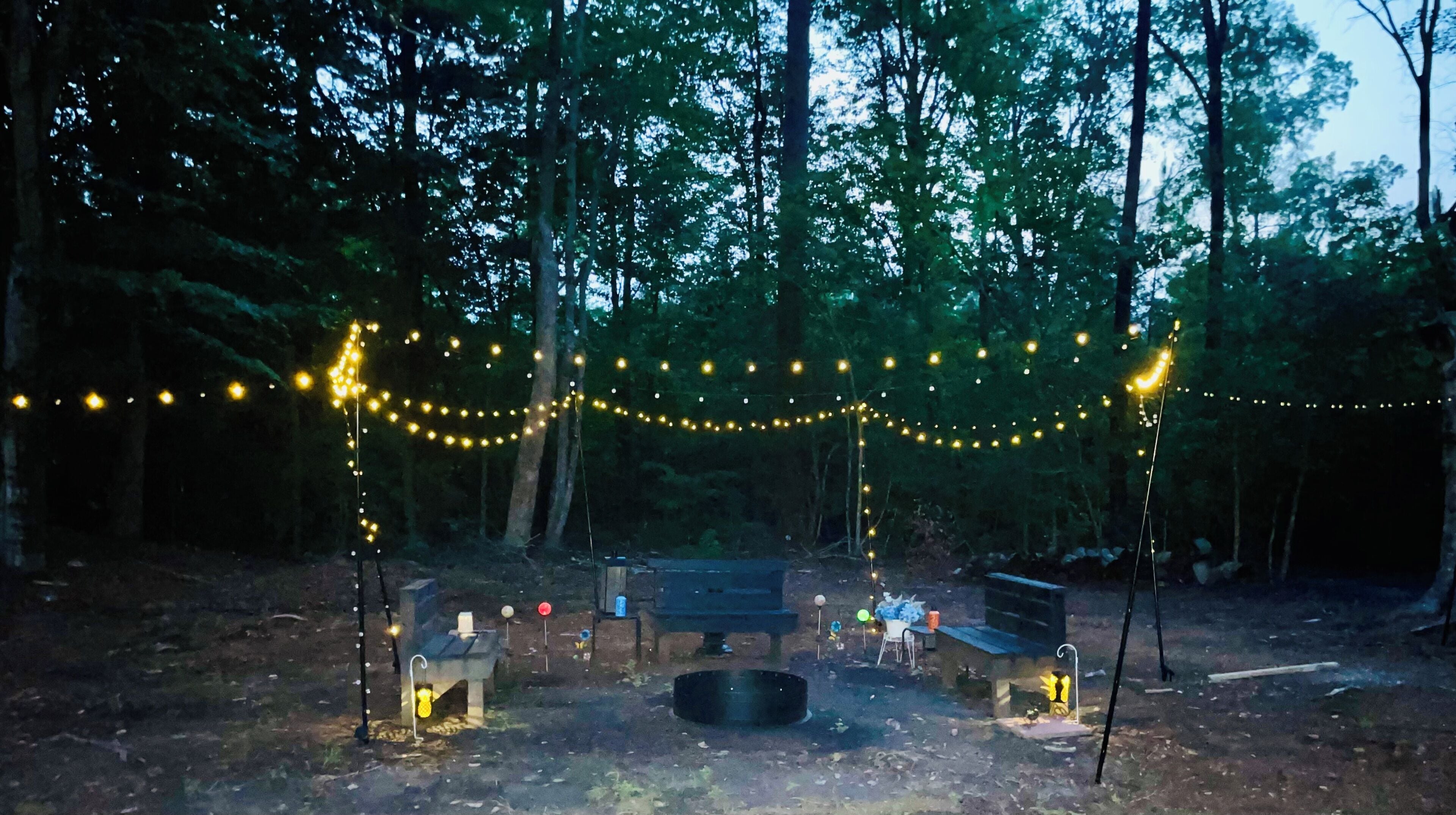 A campsite with string lights, a fire pit, and a bench.