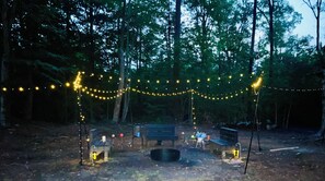 Un terrain de camping équipé de guirlandes lumineuses, d’un foyer et d’un banc.