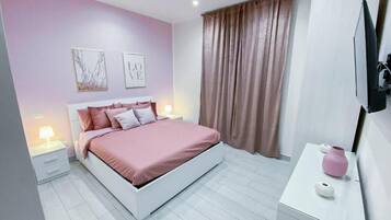 Una camera da letto con un letto, comodini, una cassettiera, una TV e una finestra con tende.