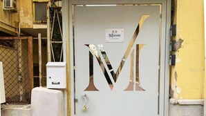 Una puerta con un gran logotipo de la letra 'M', una verja de metal y un cuadro de electricidad.