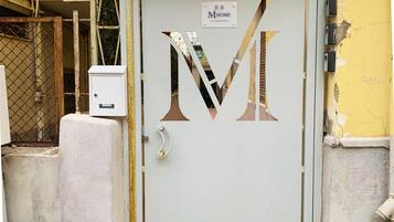 Una porta con un grande logo a forma di 'M', un cancello in metallo e un armadietto tecnico.