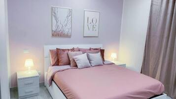 Una camera da letto con un letto, due comodini, una lampada da comodino, una parete con due quadri e una tenda.