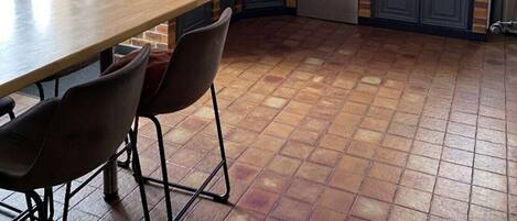 A kitchen with a brick wall, a built-in oven, a sink, and a dining area with chairs.