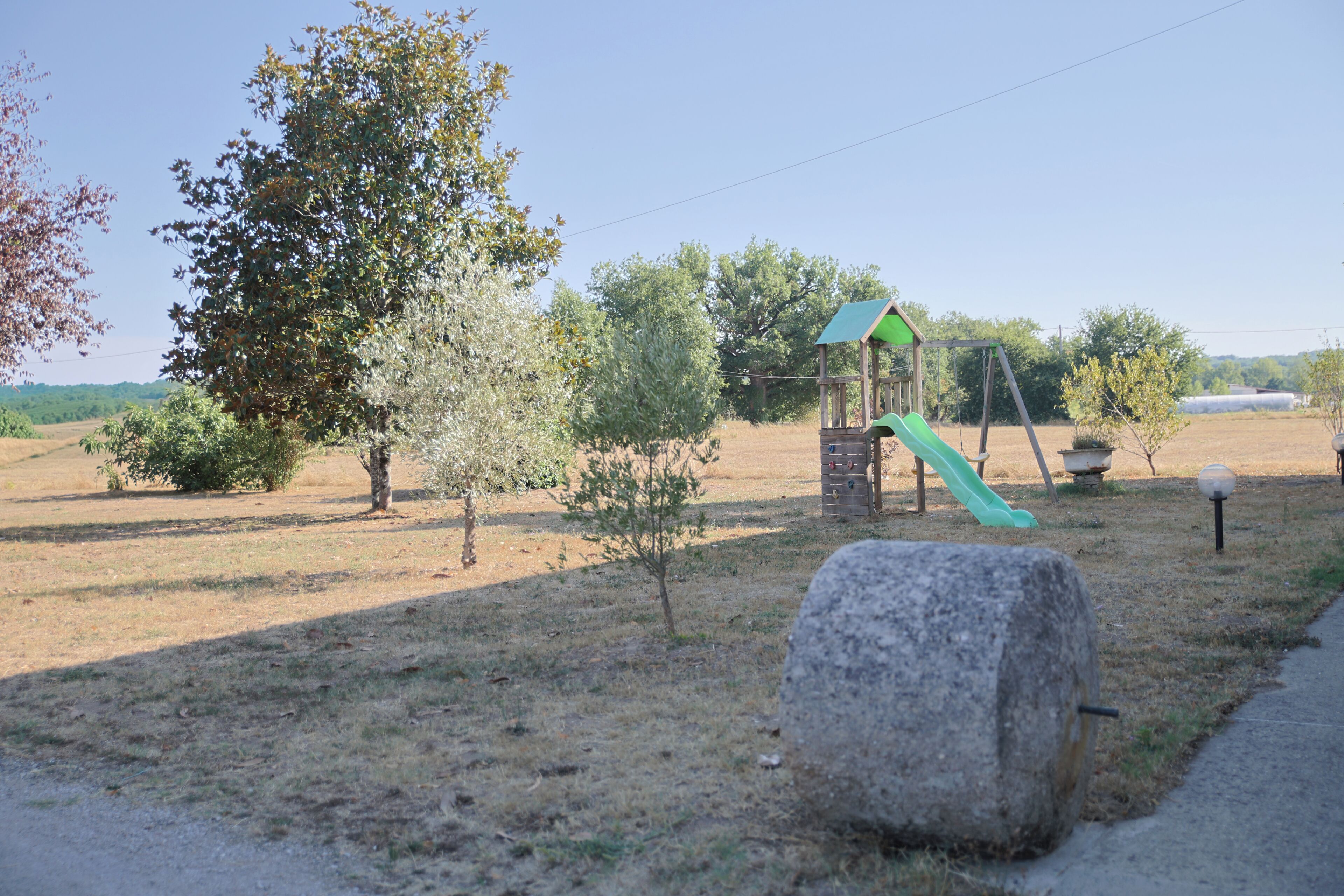 A playground with a slide and swings, surrounded by trees and open fields.