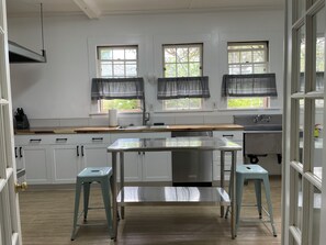 A kitchen with white cabinets, a stainless steel countertop, a sink, and two stools.
