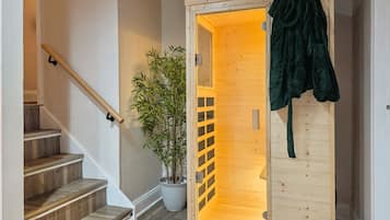 Un escalier en bois avec une rampe, un pot de bambou et une porte en bois sur laquelle est accrochée une robe verte, sur le côté droit.