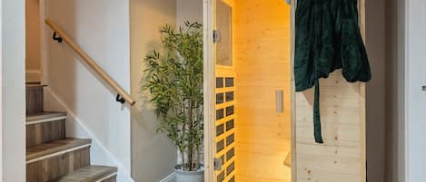 Una escalera de madera con barandilla, una planta de bambú en maceta y una puerta de madera con una bata verde colgada a la derecha.