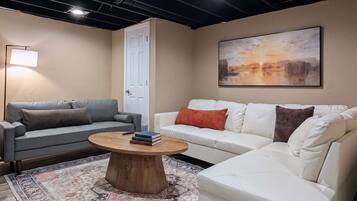 A living room with two sofas, a coffee table, a rug, a painting, and a door.