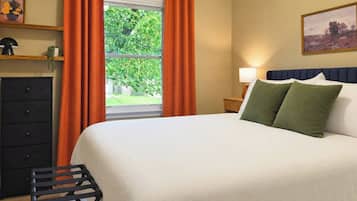 A bedroom with a bed, a nightstand, a lamp, a dresser, and a window with curtains.
