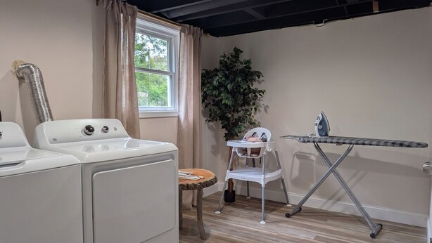 A laundry room with a washer and dryer, a folding table, and a chair. - La Petite • Piano • Serene Organic • Long Stays (Merrillville)
