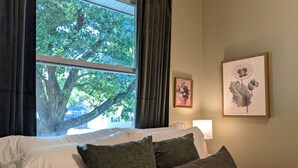 A hotel room with a bed, a window with curtains, and two framed botanical prints on the wall. - La Petite • Piano • Serene Organic • Long Stays (Merrillville)