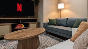 A living room with a flat-screen TV, a sofa, a coffee table, and a lamp. - La Petite • Piano • Serene Organic • Long Stays (Merrillville)