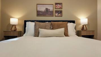A neatly made bed with a dark headboard, two bedside tables with lamps, and two framed artworks above the bed.