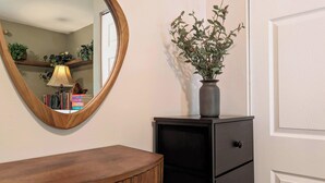 A wooden vanity with a mirror, a vase with green foliage, and a black cabinet with drawers. - La Petite • Piano • Serene Organic • Long Stays (Merrillville)